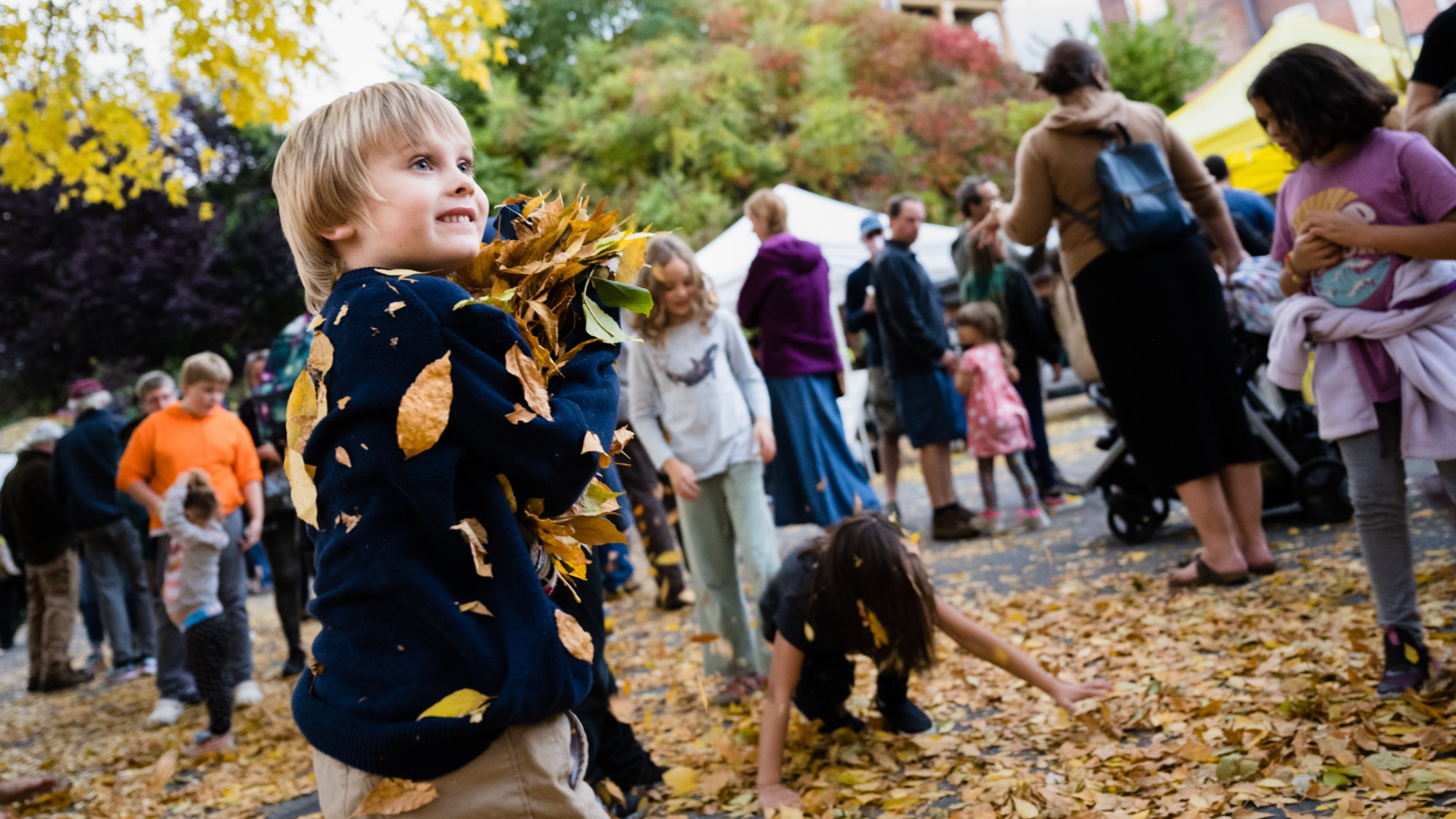 A child plays with fallen autumn leaves in the Harmony Parking Lot during a street festival.