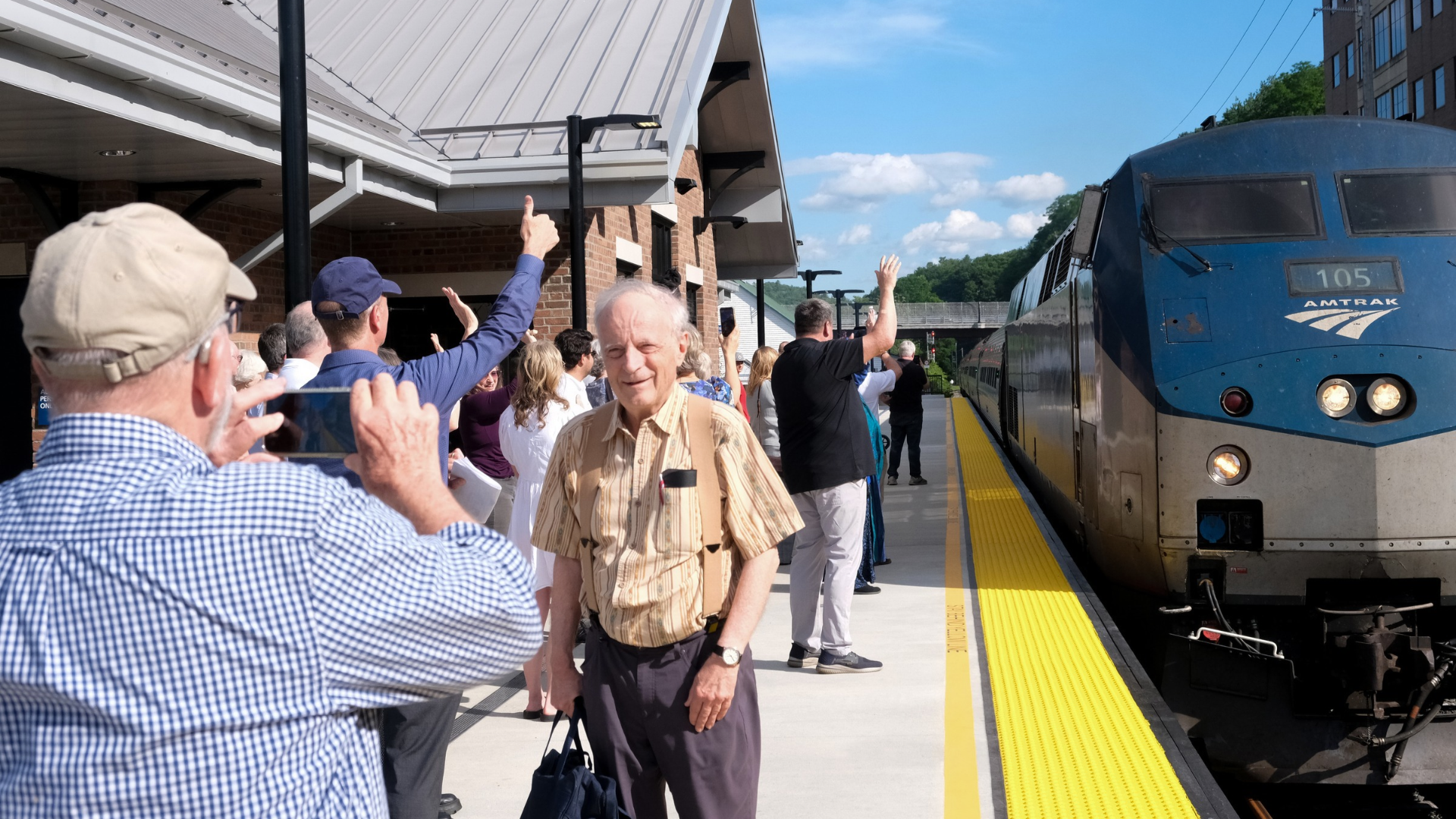 A man takes a photo of an elderly man at a crowded train station as an Amtrak Train approaches.